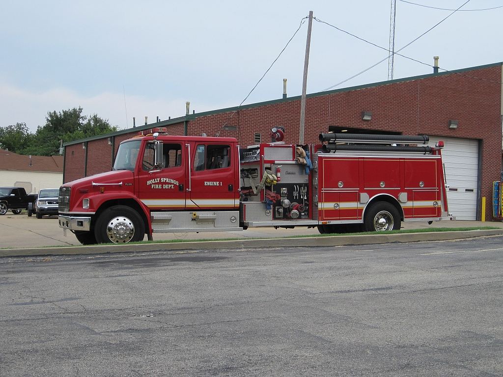 A red fire engine parked outside a red-brick fire station on a cloudy day