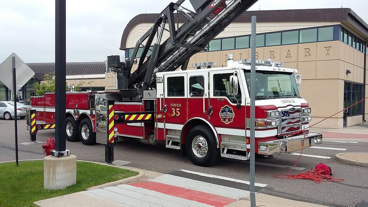 A red South Metro Fire Rescue ladder truck parked at a curb outside a library on an overcast day