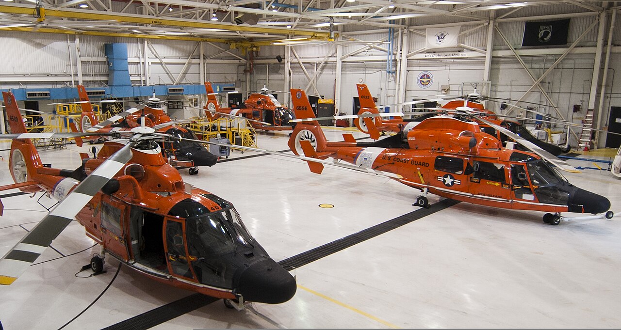 Orange U.S. Coast Guard helicopters, including one marked New Orleans, parked inside a hangar