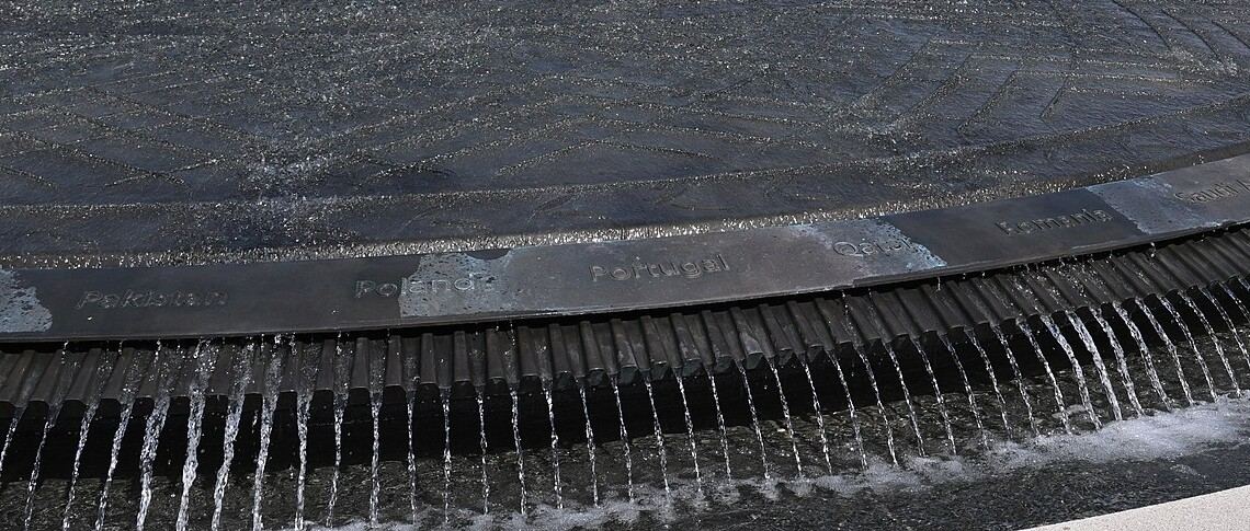 Water spills over the rim of the memorial's dark bronze shield fountain, which is engraved with the names of coalition nations