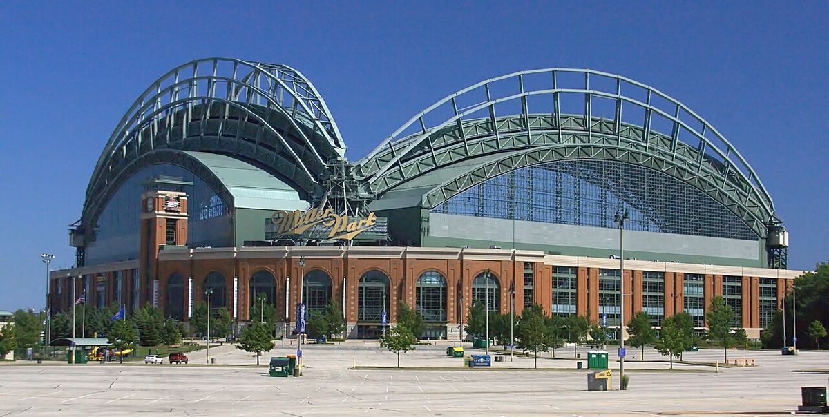 The brick-and-steel ballpark in Milwaukee, with its fan-shaped arched roof, under a clear blue summer sky