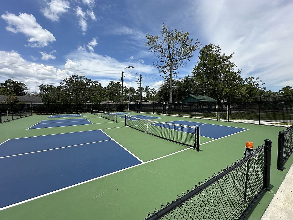 Empty blue-and-green outdoor pickleball courts with nets under a bright, partly cloudy sky