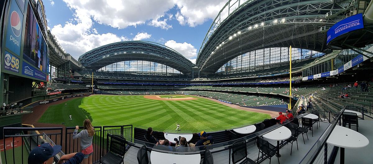 A wide view of American Family Field in Milwaukee, with its green diamond under an arched roof and a blue sky with white clouds