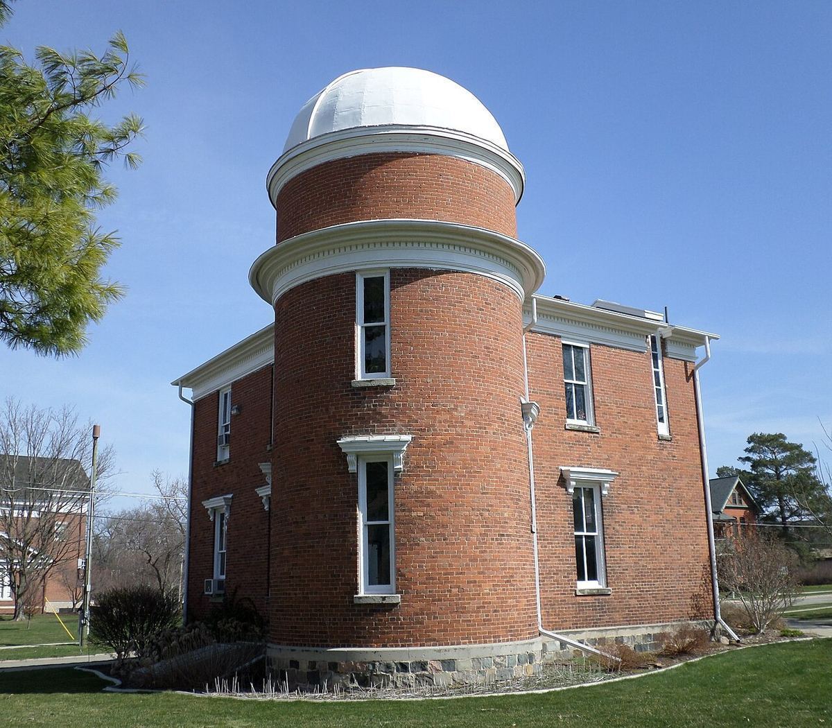 A red-brick observatory with a white dome on a green lawn at Albion College under a blue sky