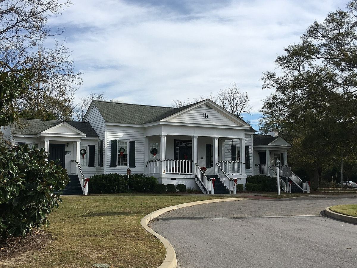 A white two-story house with a wide front porch and twin staircases, now Blythewood's town hall, under a partly cloudy sky
