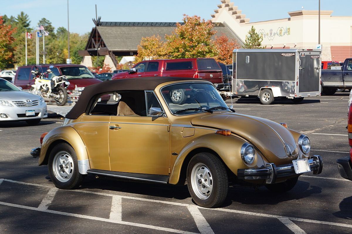 A gold 1974 Volkswagen Beetle convertible with its top up, parked in a sunny lot
